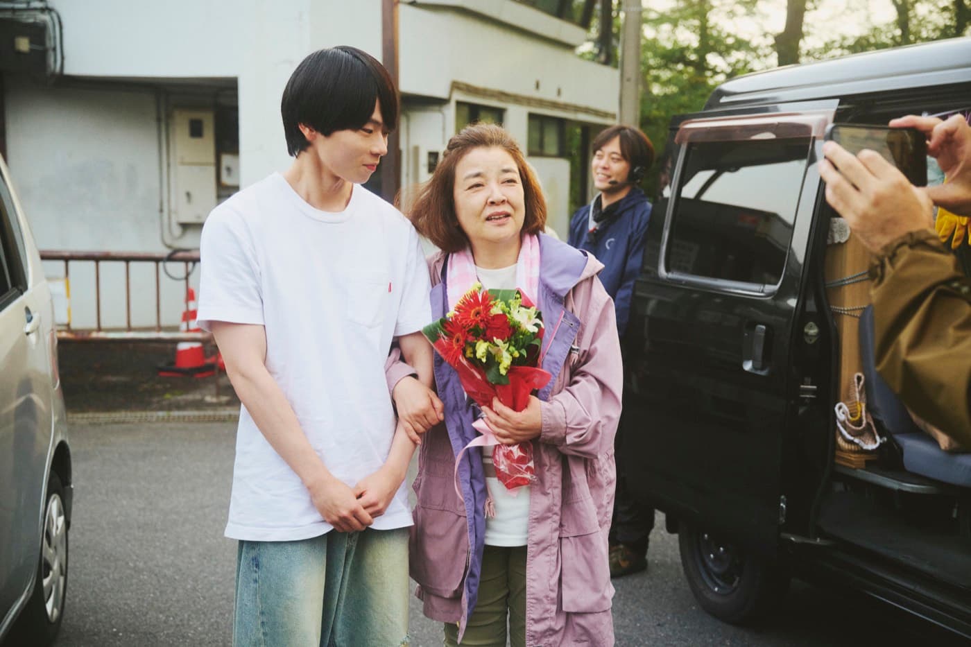 花束を手に見送られる撮影終了の場面